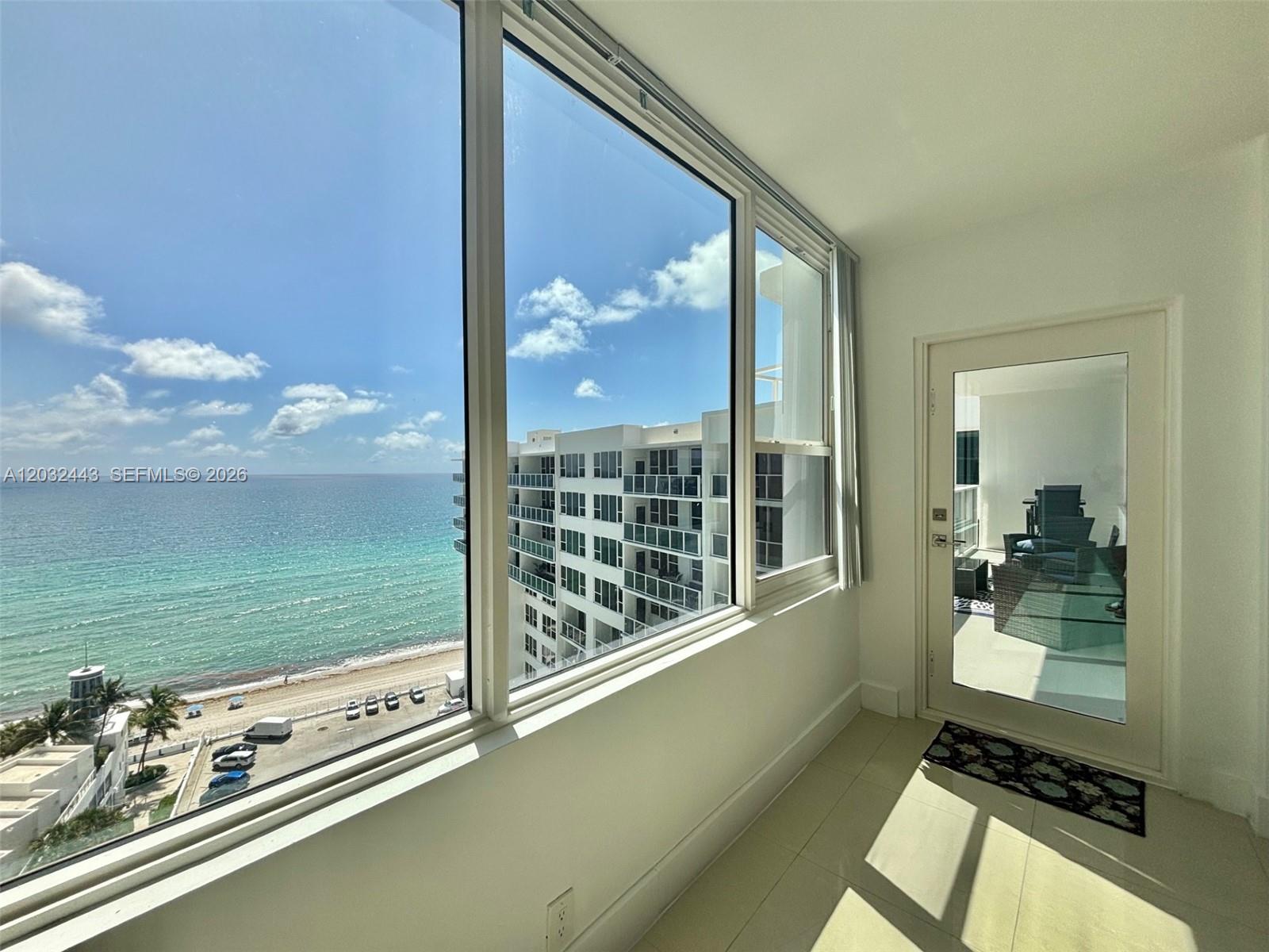 A sunlit room features large windows overlooking the ocean, a beach, and a neighboring building — 3505 S Ocean Dr # 1506, Hollywood FL 33019, HOLLYWOOD, FL