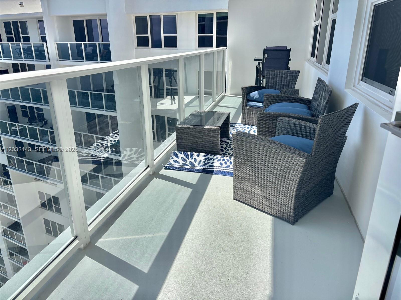 A balcony features gray wicker furniture with blue cushions and a patterned outdoor rug — 3505 S Ocean Dr # 1506, Hollywood FL 33019, HOLLYWOOD, FL