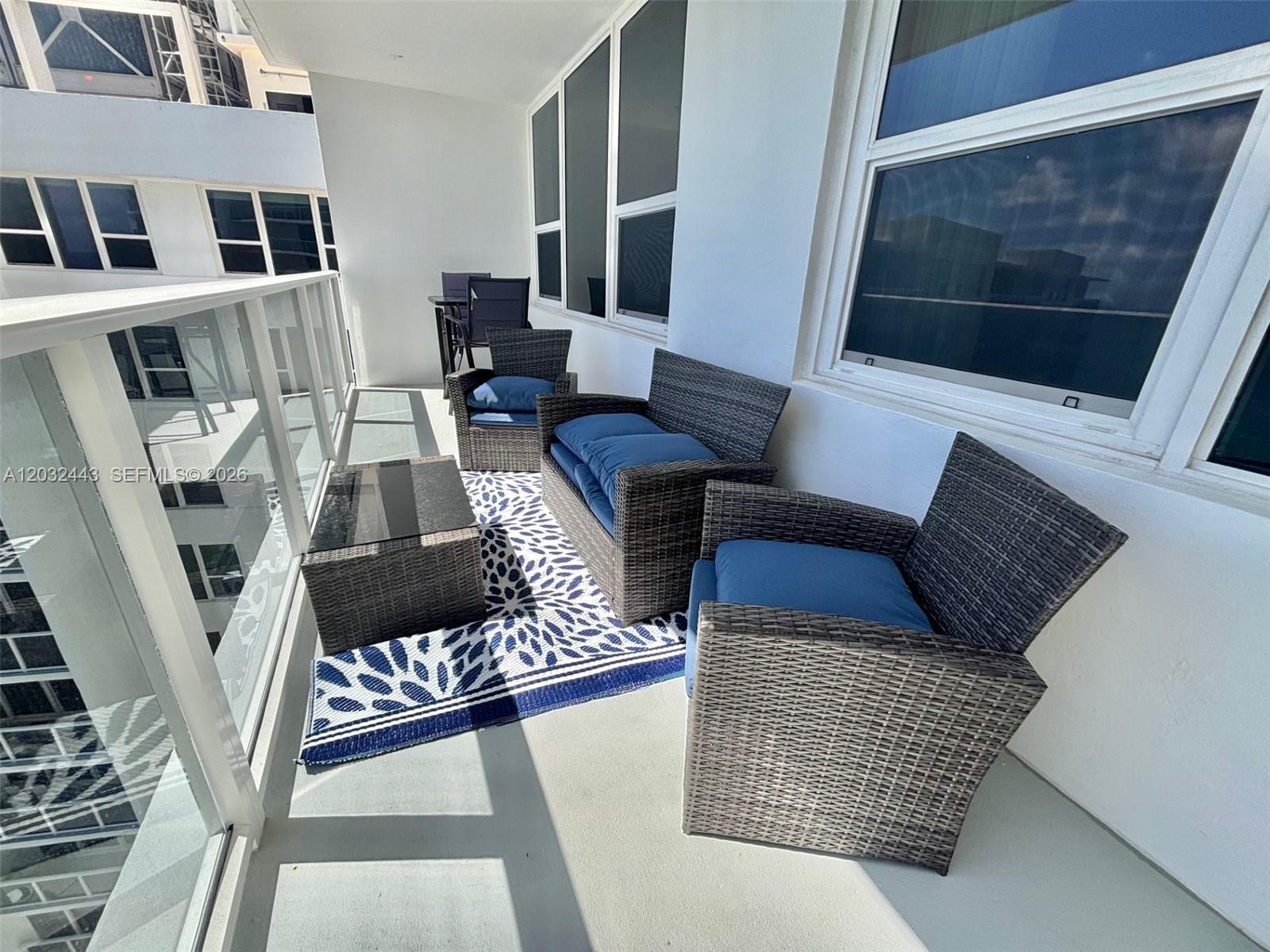 A balcony features wicker furniture with blue cushions and a patterned rug — 3505 S Ocean Dr # 1506, Hollywood FL 33019, HOLLYWOOD, FL