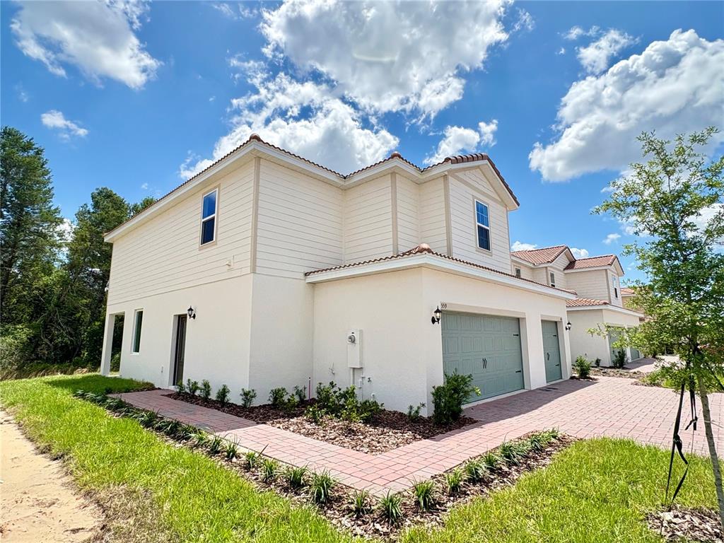 A two-story townhouse with a light-colored exterior, a green garage door, and brick pavers — 559 BAY LEAF DRIVE, POINCIANA, FL