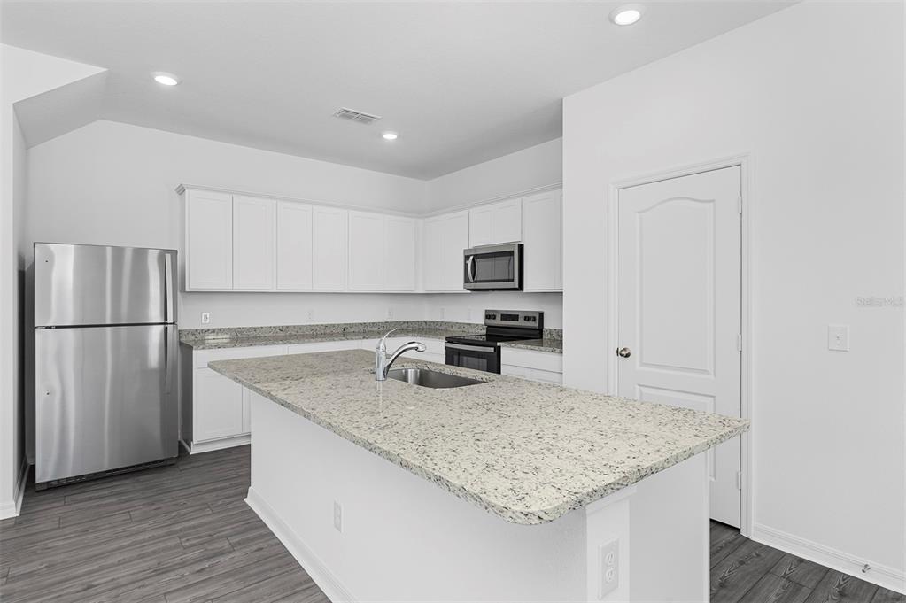 A kitchen features white cabinets, granite countertops, a center island, and stainless steel appliances — 559 BAY LEAF DRIVE, POINCIANA, FL