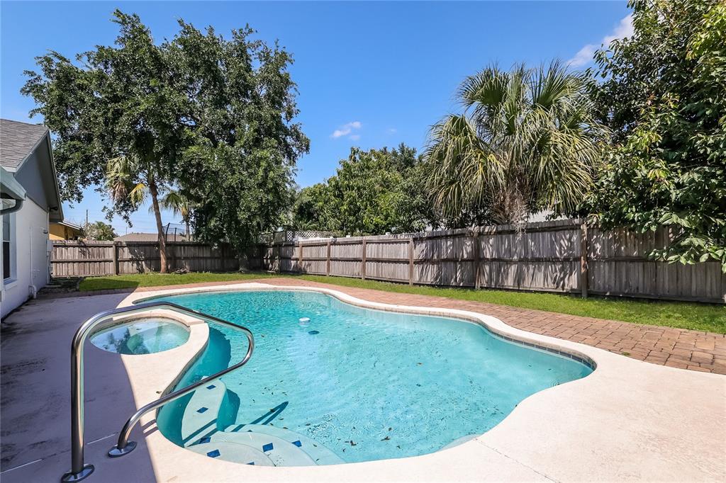 A backyard features a kidney-shaped swimming pool with a built-in spa and a wooden fence — 12013 CLOVE STREET, ORLANDO, FL