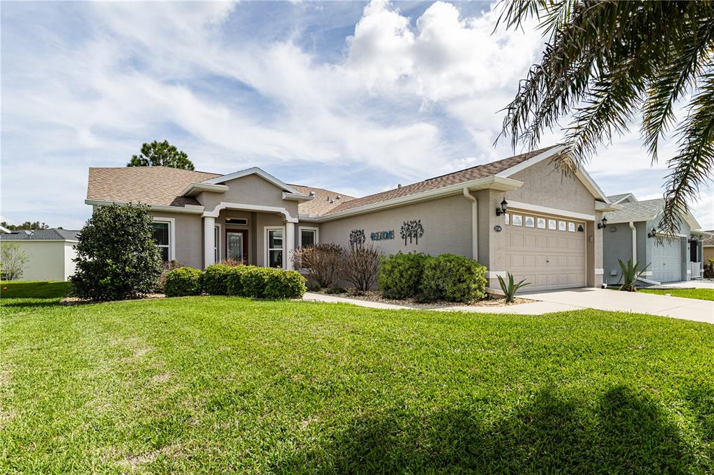 A single-story suburban house with a tan stucco exterior, a two-car garage, and green lawn — 27118 ROANOKE DRIVE, LEESBURG, FL