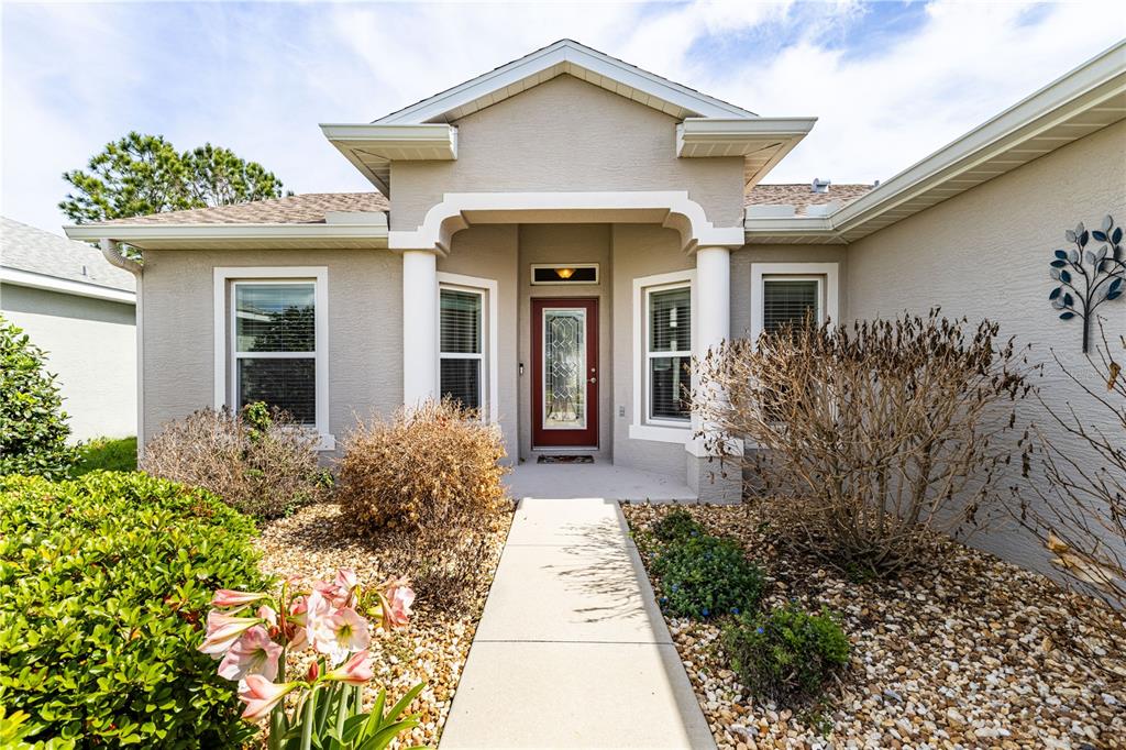 A beige house exterior features a red front door, white columns, and a concrete walkway — 27118 ROANOKE DRIVE, LEESBURG, FL