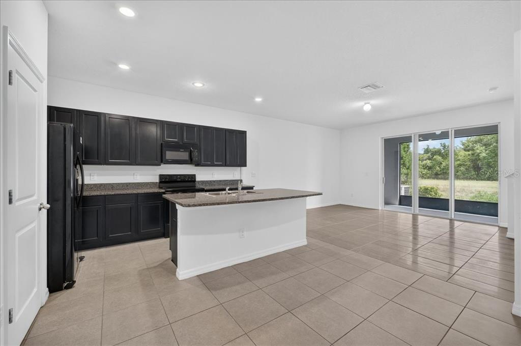 A kitchen with dark cabinets, granite countertops, and an island opens to a tiled living area — 8655 FALLING BLUE PLACE, RIVERVIEW, FL