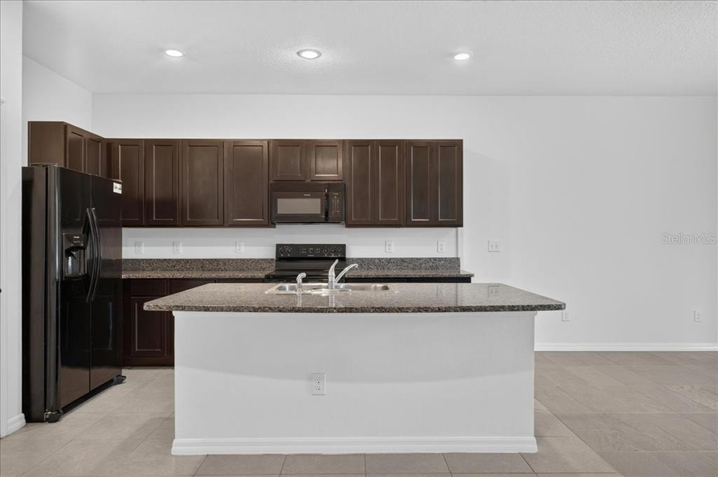 A kitchen features dark wood cabinets, granite countertops, a central island, and black appliances — 8655 FALLING BLUE PLACE, RIVERVIEW, FL