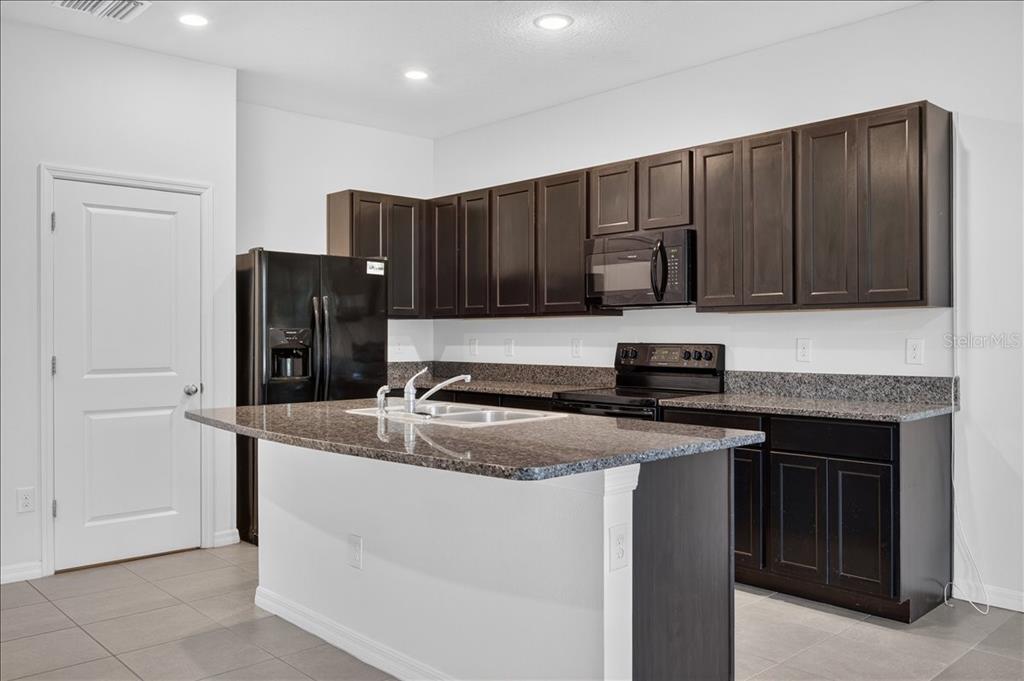 A kitchen features dark wood cabinets, granite countertops, a central island, and black appliances — 8655 FALLING BLUE PLACE, RIVERVIEW, FL