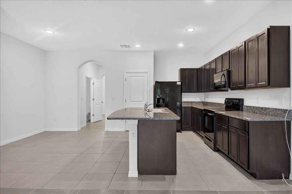 A kitchen features dark wood cabinets, granite countertops, a center island, and tile flooring — 8655 FALLING BLUE PLACE, RIVERVIEW, FL