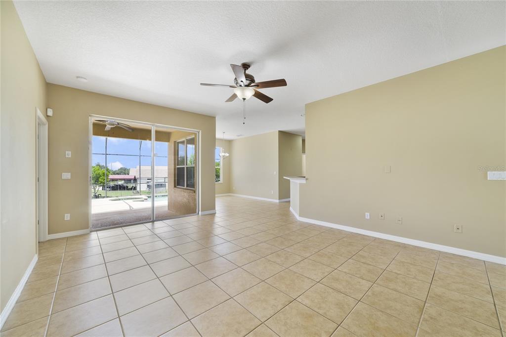 An open-concept living area features beige tile flooring, tan walls, and sliding glass patio doors — 243 WILDFLOWER ROAD, DAVENPORT, FL