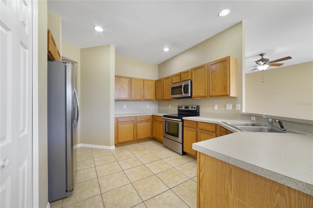 A kitchen features oak cabinets, stainless steel appliances, tile flooring, and a breakfast bar — 243 WILDFLOWER ROAD, DAVENPORT, FL