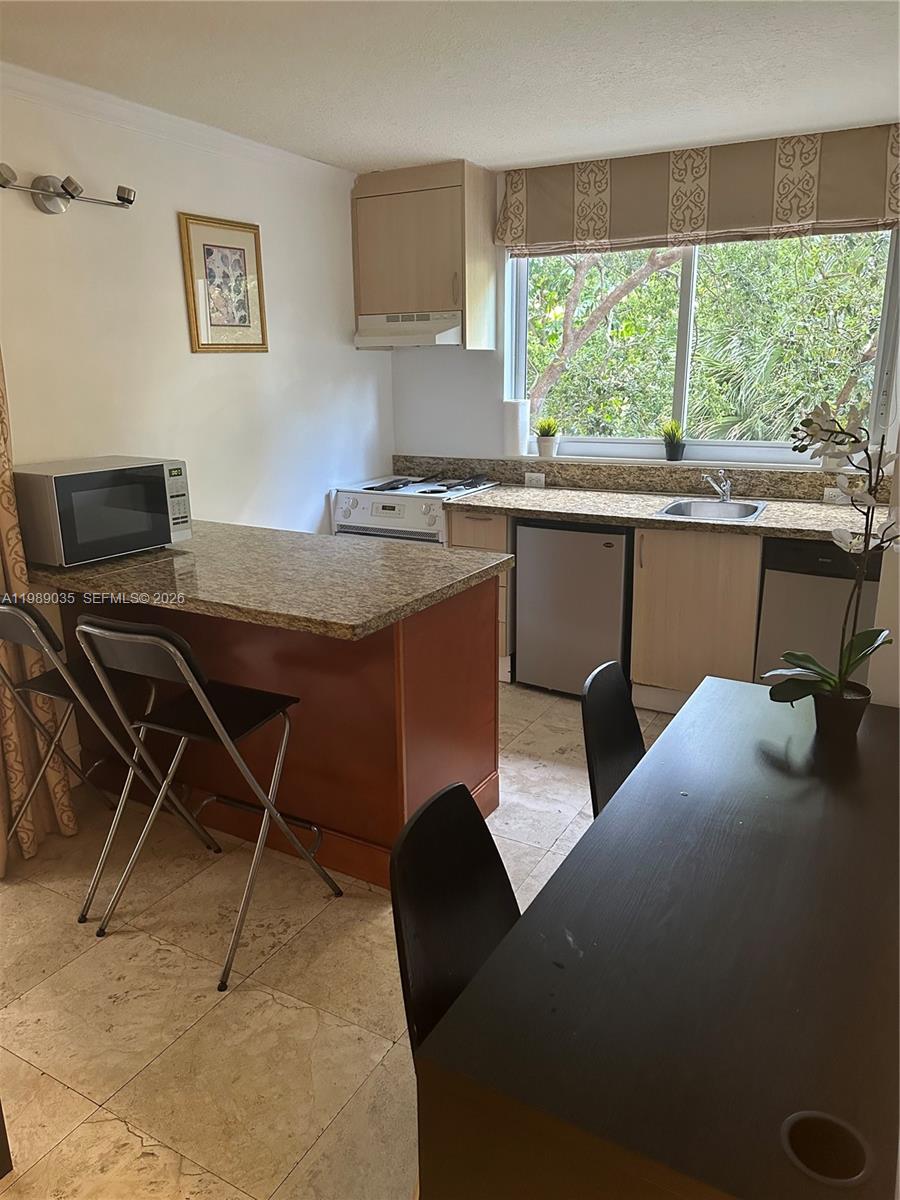 This kitchen features granite countertops, light wood cabinets, a small dining area, and tile flooring — 2951 S Bayshore Dr # 417, Miami FL 33133, MIAMI, FL
