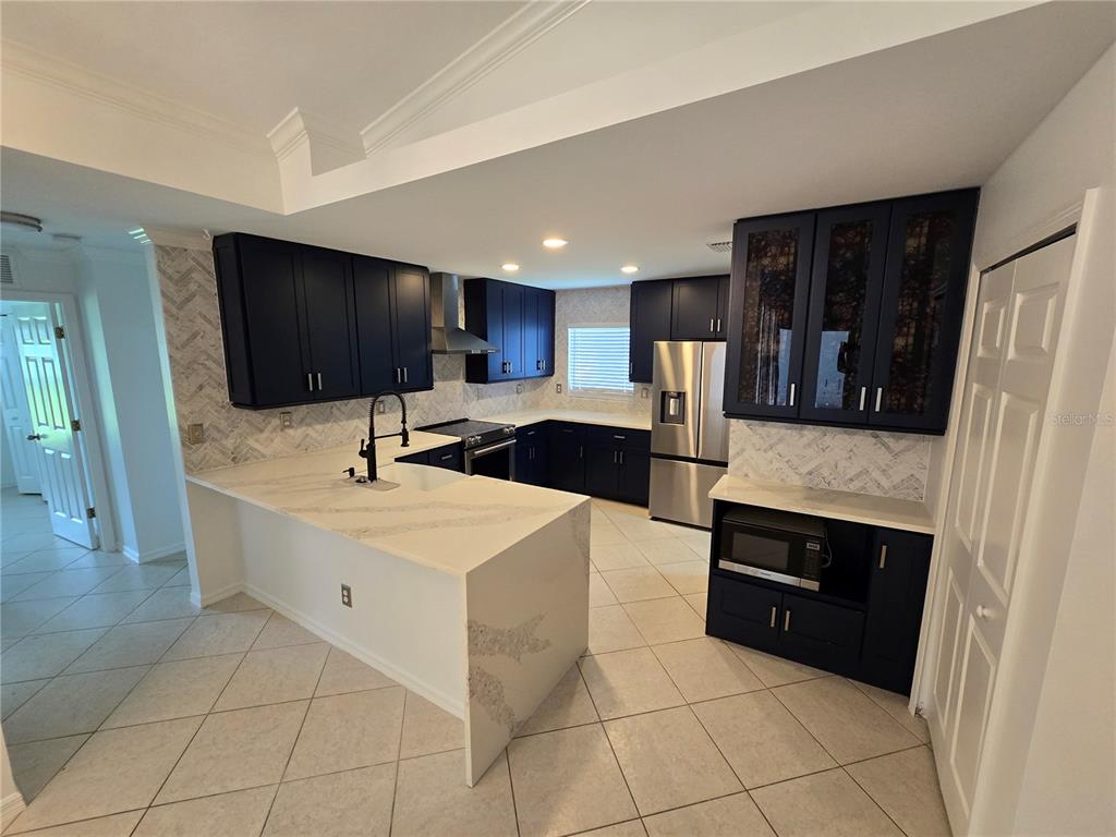 A kitchen features dark blue cabinets, white quartz countertops, and a herringbone-patterned tile backsplash — 219 NW 25TH PLACE, CAPE CORAL, FL
