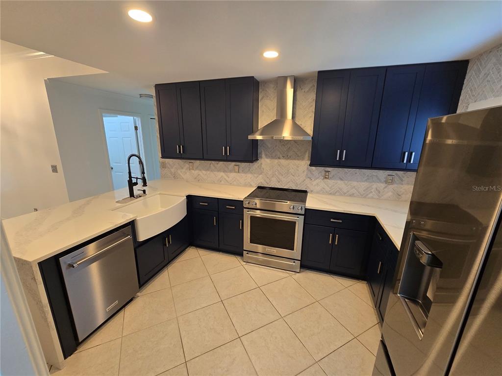 A kitchen features dark blue cabinets, stainless steel appliances, a farmhouse sink, and white countertops — 219 NW 25TH PLACE, CAPE CORAL, FL