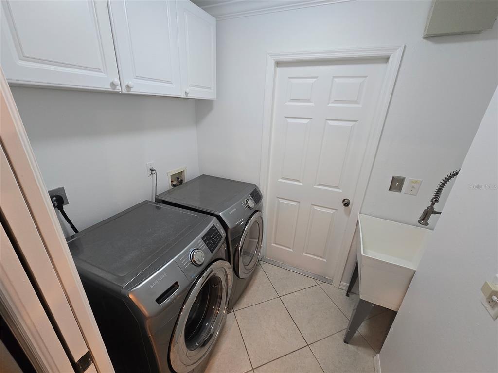 A laundry room features grey Samsung appliances, white cabinets, a utility sink, and tiled flooring — 219 NW 25TH PLACE, CAPE CORAL, FL
