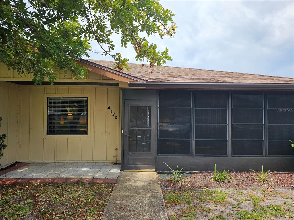 The exterior of a house features a tan wall, a screened porch, and a walkway — 4132 66TH STREET CIRCLE W, BRADENTON, FL