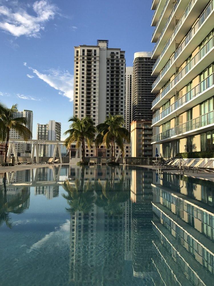 A swimming pool reflects surrounding high-rise apartment buildings and palm trees under a blue sky — 1111 SW 1st Ave, Miami FL 33130, MIAMI, FL