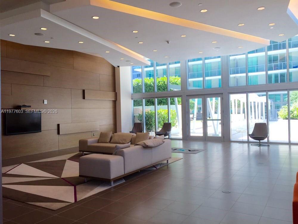 A modern lobby features a large sectional sofa, wood-paneled walls, and floor-to-ceiling glass windows — 1111 SW 1st Ave, Miami FL 33130, MIAMI, FL