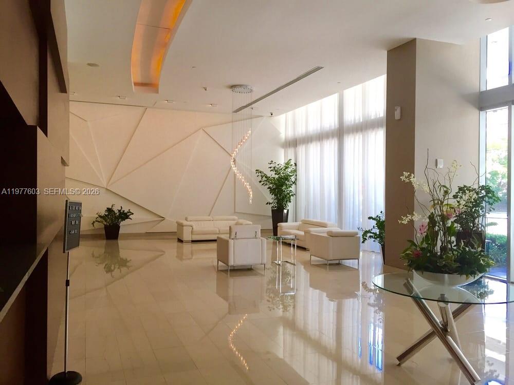 A modern lobby features white leather furniture, geometric wall paneling, and large floor-to-ceiling windows — 1111 SW 1st Ave, Miami FL 33130, MIAMI, FL