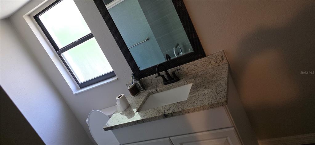 A bathroom features a granite vanity countertop, a dark-framed mirror, and a window — 10021 CHERRY CREEK LANE, PORT RICHEY, FL
