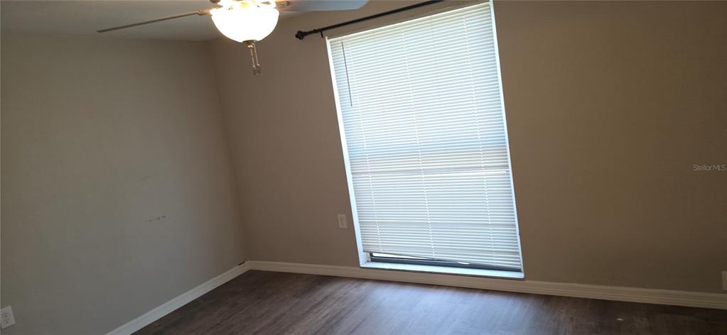 An empty bedroom features light gray walls, wood-look flooring, a ceiling fan, and a window — 10021 CHERRY CREEK LANE, PORT RICHEY, FL