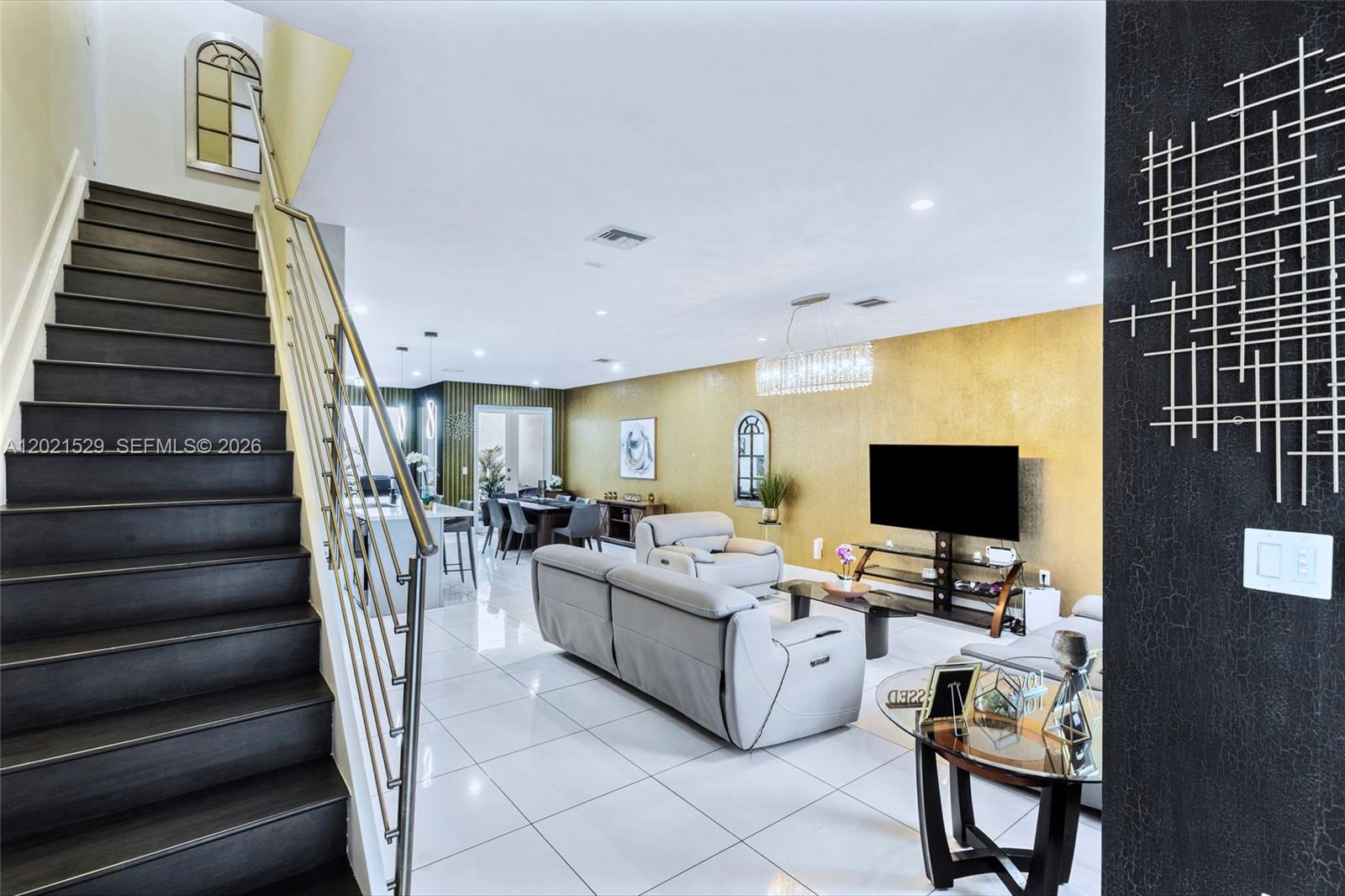 A modern living room features a gold accent wall, white tile floors, and a staircase — 6400 NW 105th Pl, Doral FL 33178, DORAL, FL
