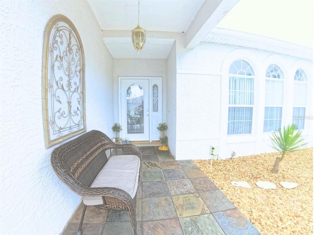 A covered entryway features a wicker bench, tiled flooring, and a white front door — 5340 NW 26TH LANE, OCALA, FL