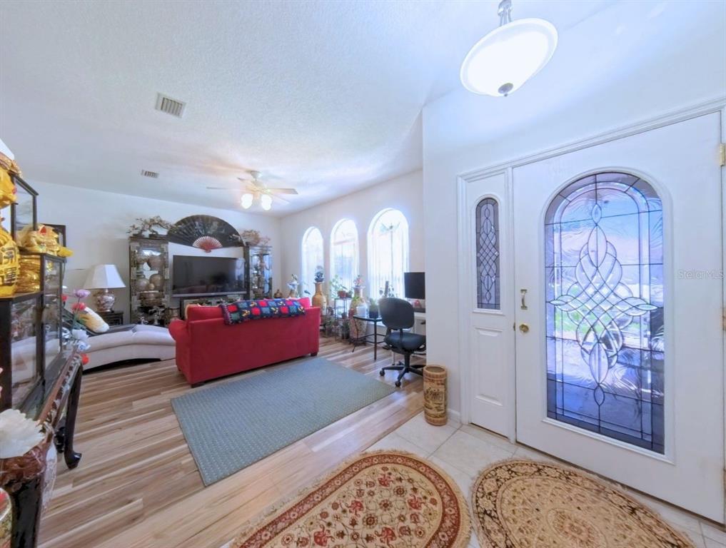A living room with wood-look flooring, a red sofa, and an arched glass front door — 5340 NW 26TH LANE, OCALA, FL