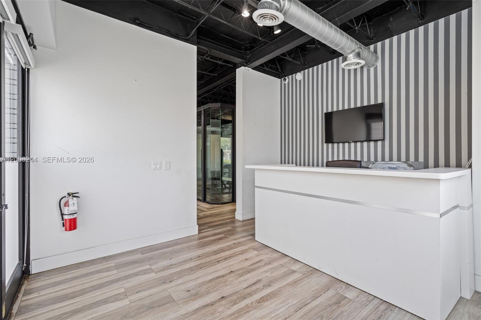 A reception area features a white desk, striped wallpaper, and an exposed black ceiling — 4885 NW 7th Ave, Miami FL 33127, MIAMI, FL