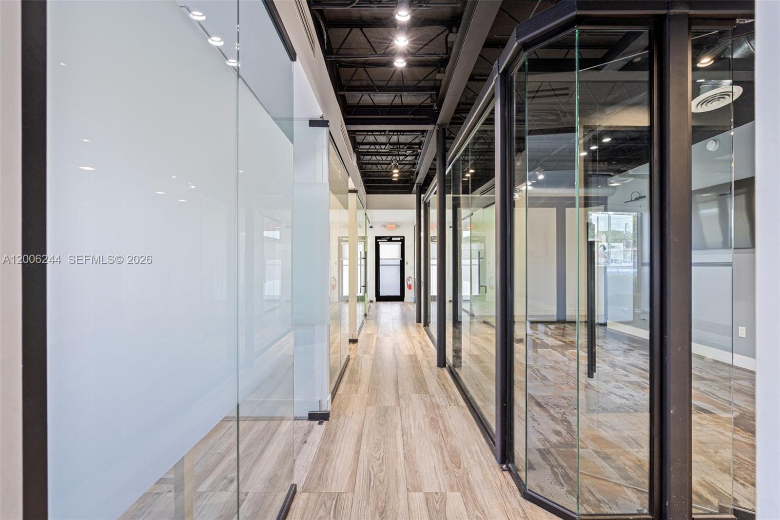 A hallway with wood-look flooring leads to a glass door between glass-walled office spaces — 4885 NW 7th Ave, Miami FL 33127, MIAMI, FL