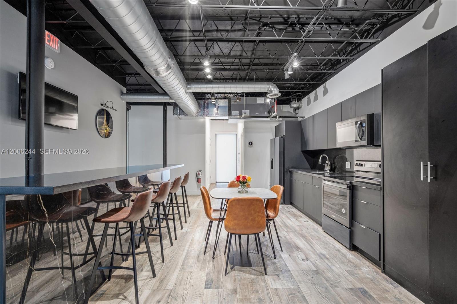 A modern kitchen and dining area features dark cabinetry, exposed ductwork, and wood-look flooring — 4885 NW 7th Ave, Miami FL 33127, MIAMI, FL