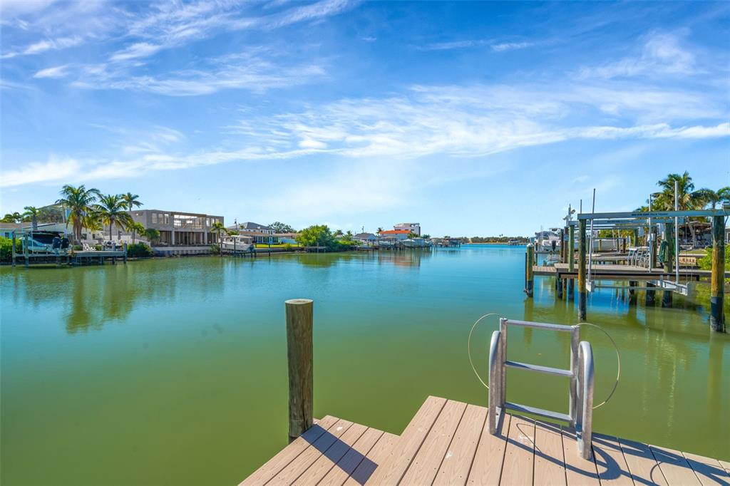 A wooden boat dock overlooks a calm canal with houses and palm trees in the distance — 7932 2ND AVENUE S, ST PETERSBURG, FL