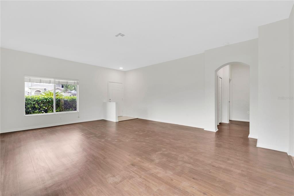An empty living room with light wood-look flooring, white walls, and an arched entryway — 25702 ALDUS DRIVE, LAND O LAKES, FL