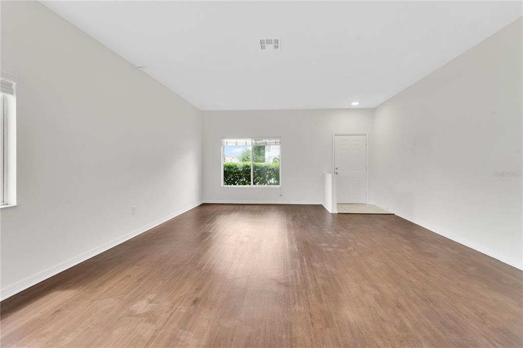 An empty room features light walls, dark wood-look flooring, a window, and a white door — 25702 ALDUS DRIVE, LAND O LAKES, FL