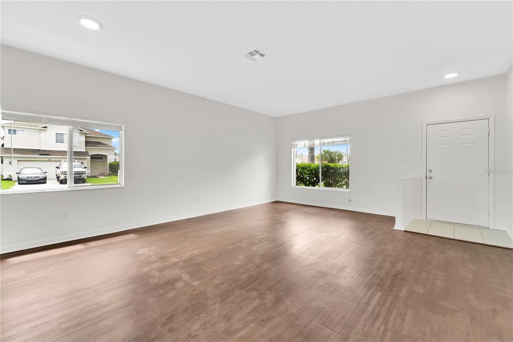 An empty living room features light-colored walls, wood-look tile flooring, recessed lighting, and two windows — 25702 ALDUS DRIVE, LAND O LAKES, FL