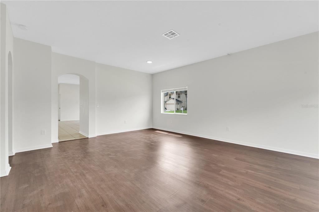 An empty room with light gray walls, dark wood-look flooring, and an arched doorway — 25702 ALDUS DRIVE, LAND O LAKES, FL