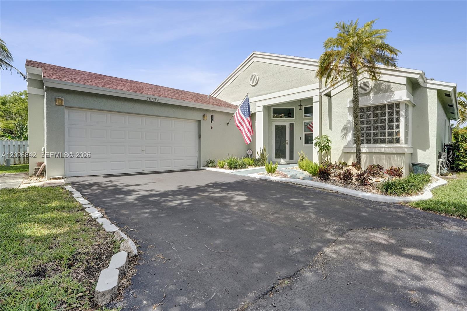 A single-story house with a garage, a palm tree, and an American flag — 10639 Lago Welleby Dr, Sunrise FL 33351, SUNRISE, FL