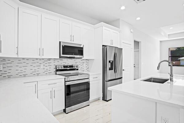 A modern kitchen features white cabinetry, stainless steel appliances, and a white quartz island — 4709 Seagrape Drive, Fort Pierce FL 34945, FORT PIERCE, FL