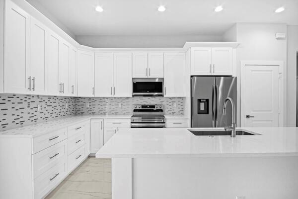 A modern white kitchen features stainless steel appliances, quartz countertops, and a tiled backsplash — 4709 Seagrape Drive, Fort Pierce FL 34945, FORT PIERCE, FL