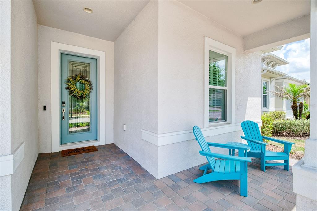 A covered front porch features a light blue door, brick pavers, and two blue chairs — 1981 FLORA PASS PLACE, KISSIMMEE, FL