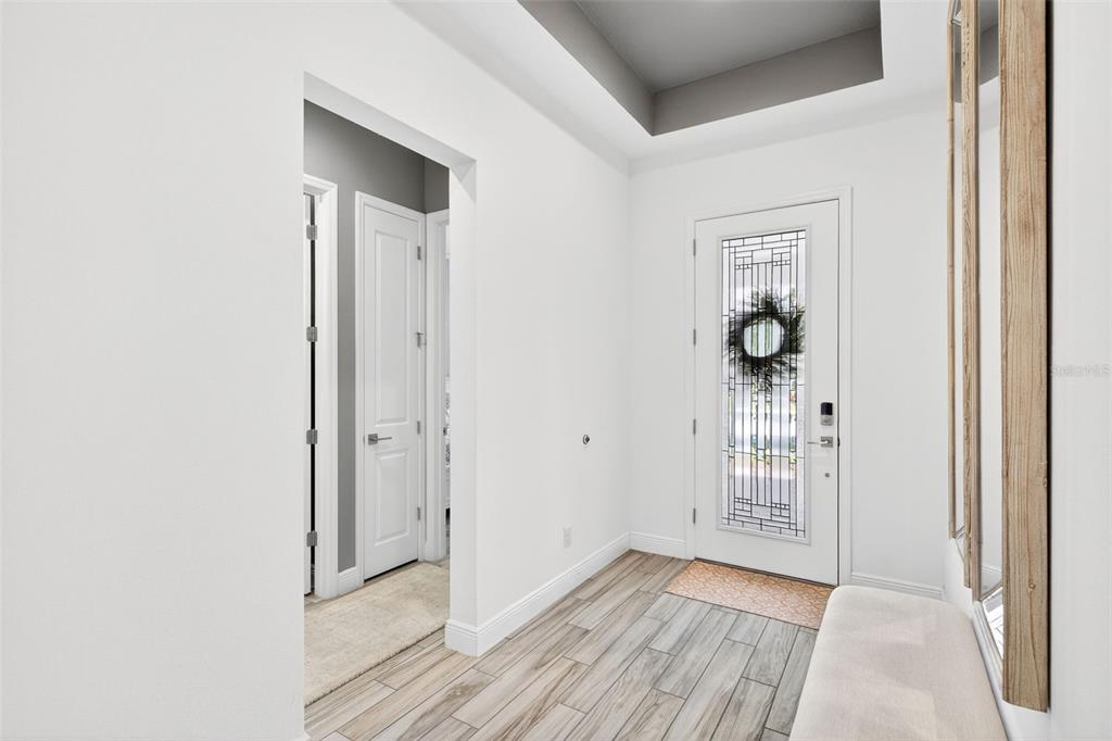 A bright entryway features wood-look tile flooring, a white front door, and a recessed ceiling — 1981 FLORA PASS PLACE, KISSIMMEE, FL