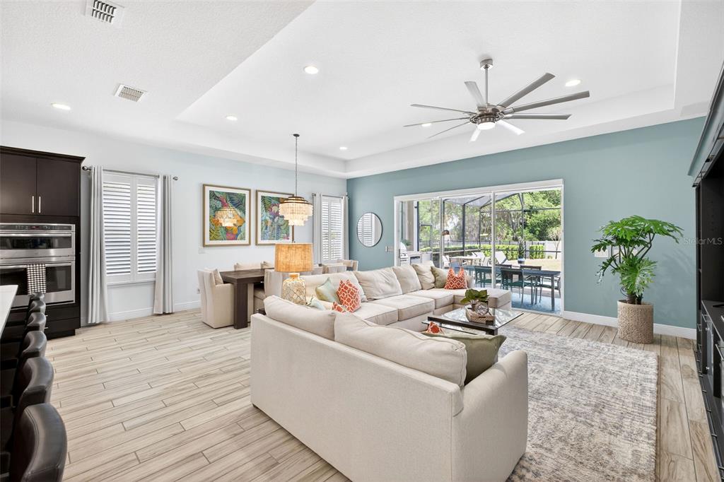 A spacious open-concept living room features a large sectional sofa, dining area, and sliding glass doors — 1981 FLORA PASS PLACE, KISSIMMEE, FL