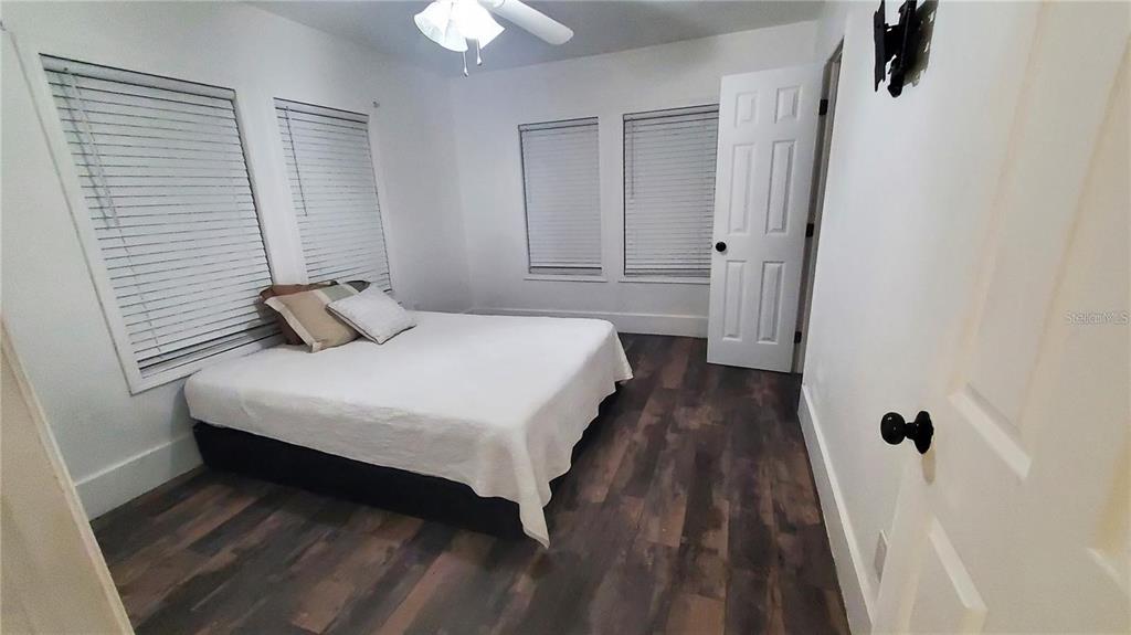 A bedroom features white walls, dark wood-look flooring, a bed, and several windows with blinds — 1034 16TH AVENUE S, ST PETERSBURG, FL