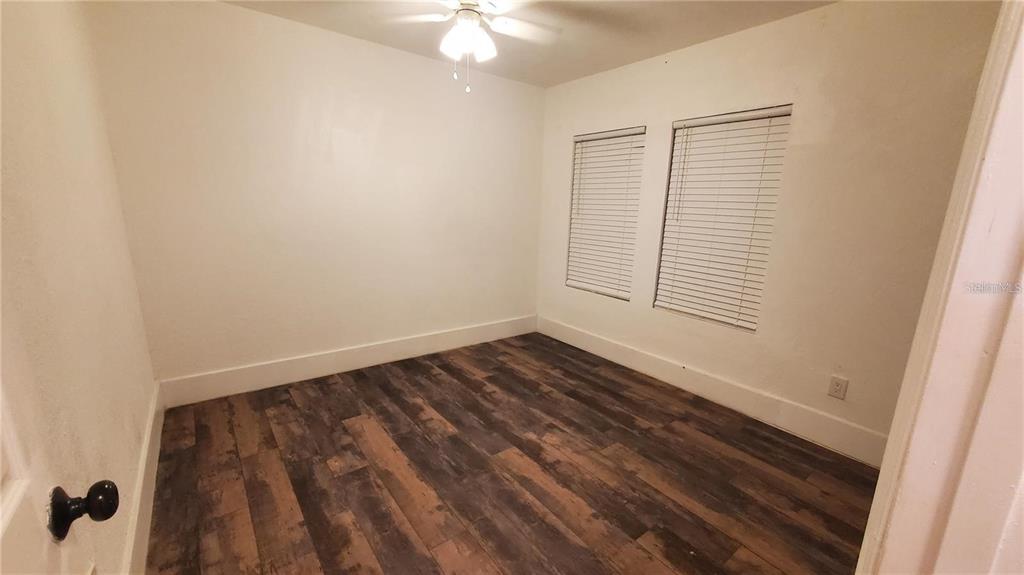 An empty bedroom features white walls, dark wood-look flooring, and two windows with blinds — 1034 16TH AVENUE S, ST PETERSBURG, FL