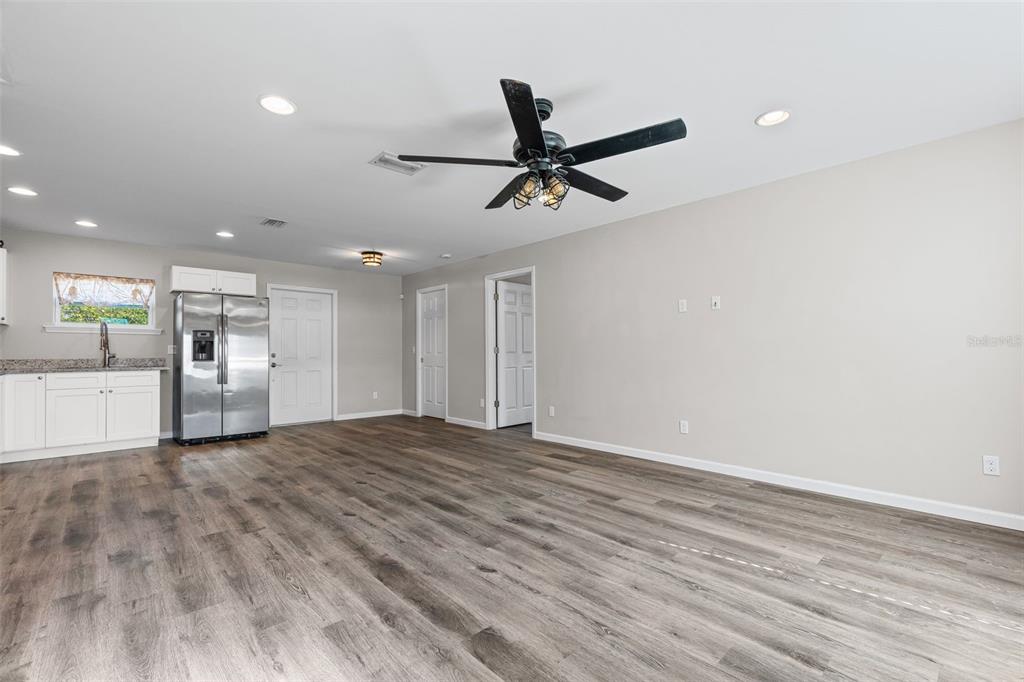 A spacious room features light gray walls, wood-look flooring, a ceiling fan, and a kitchen area — 18386 LOCKLANE AVENUE, PORT CHARLOTTE, FL