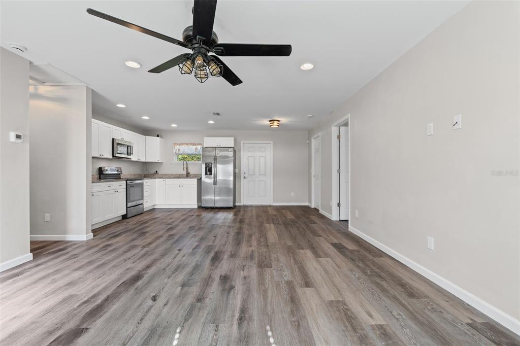 An open-concept kitchen and living area features white cabinets, stainless steel appliances, and wood-look flooring — 18386 LOCKLANE AVENUE, PORT CHARLOTTE, FL