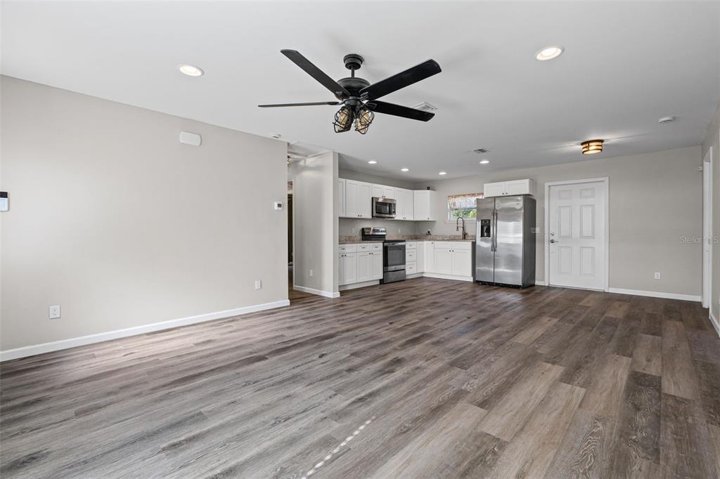 An open-concept kitchen and living area features wood-look flooring, white cabinetry, and stainless steel appliances — 18386 LOCKLANE AVENUE, PORT CHARLOTTE, FL