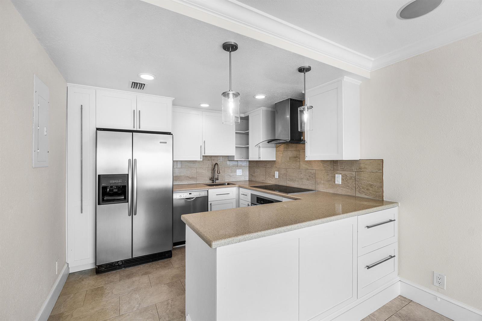 A kitchen features white cabinetry, stainless steel appliances, a stone countertop, and a tile backsplash — 250 S Ocean Boulevard # 253, Delray Beach FL 33483, DELRAY BEACH, FL