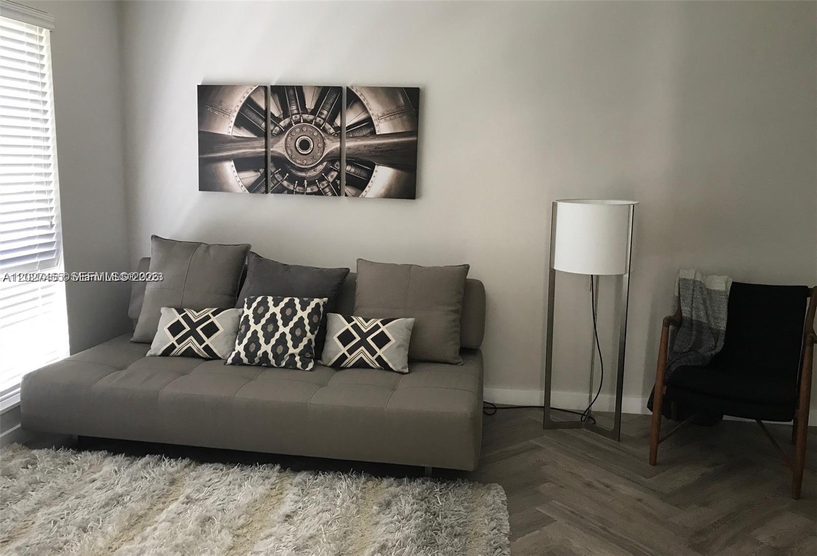 A living room features a gray sofa, a floor lamp, and wall art — 9920 Collins Ave # 1, Bal Harbour FL 33154, BAL HARBOUR, FL