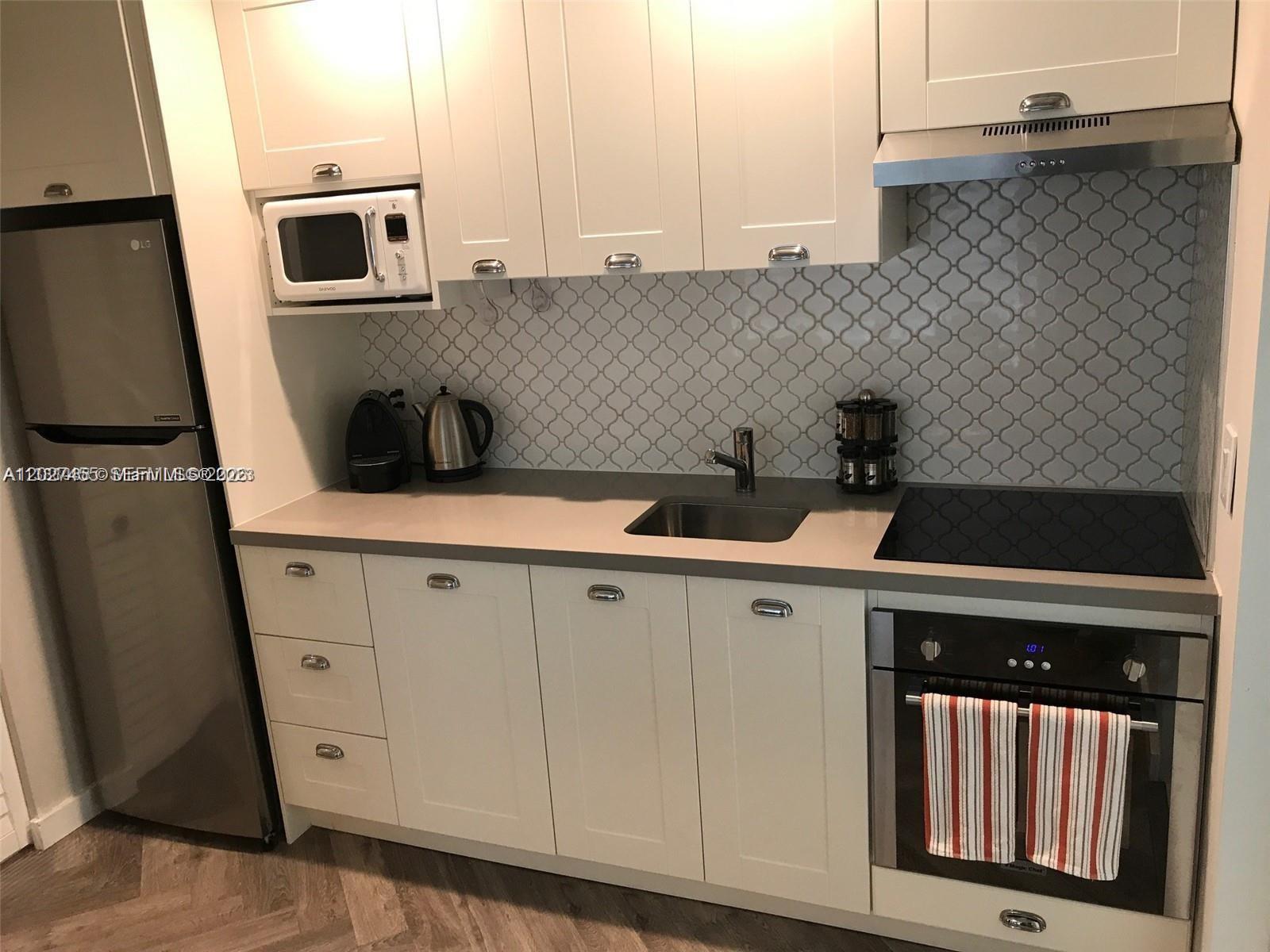 A compact kitchen features white cabinets, stainless steel appliances, and a patterned tile backsplash — 9920 Collins Ave # 1, Bal Harbour FL 33154, BAL HARBOUR, FL