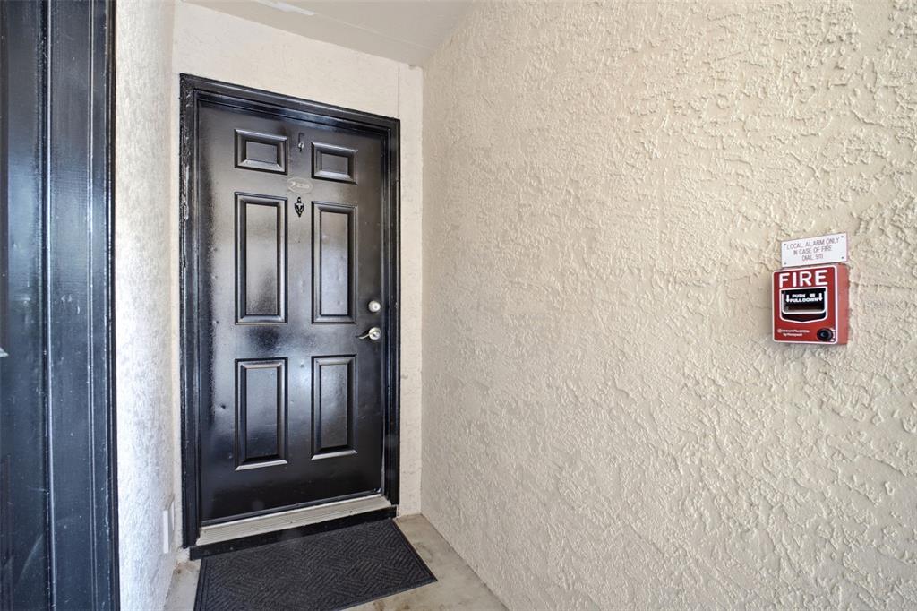 A black front door with a fire alarm pull station mounted on the textured wall — 2400 FEATHER SOUND DRIVE UNIT 236, CLEARWATER, FL